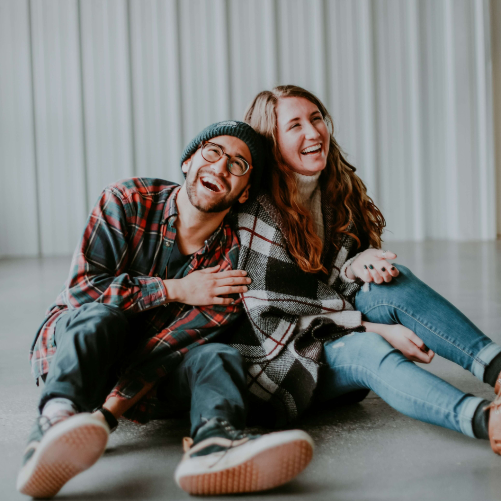 2 persons sitting on the ground laughing as a visual representation of the joy that laughter brings.