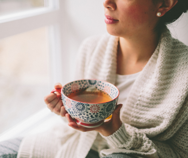 person sitting and looking out the window holding a cup of tea as a visual representation of an everyday act of self-love