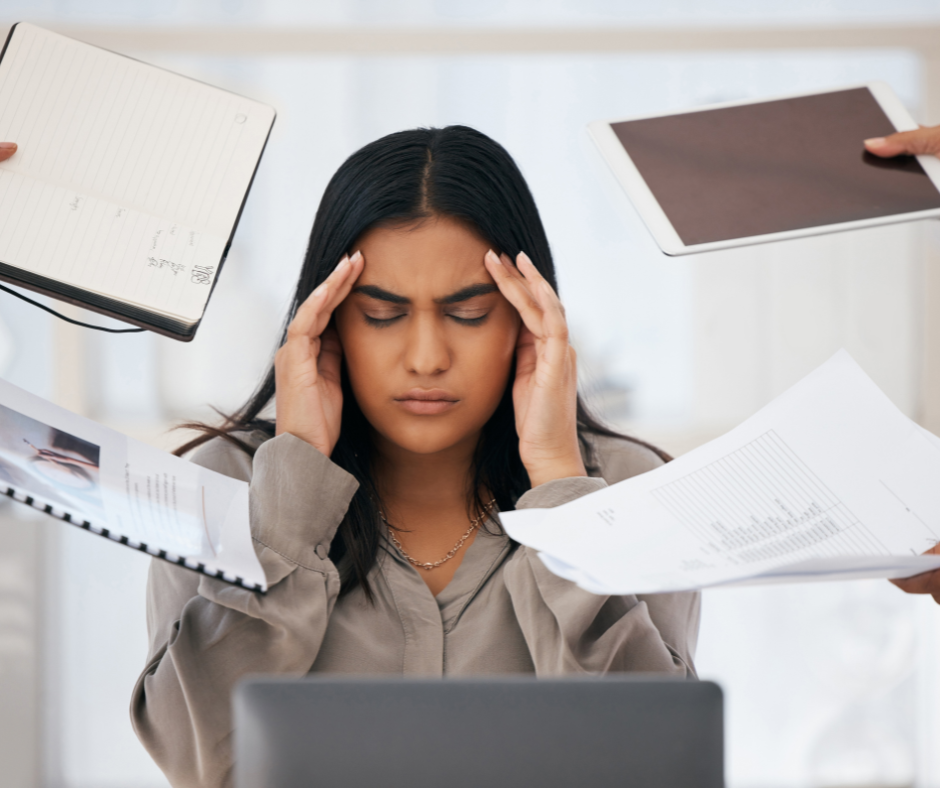 person holding their head surrounded by demanding paper work as a visual representation of occupational burnt out.