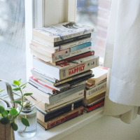 books piled on window sill with a plant on the side as a visual representation the books recommended by Uthando School on the journey to self-love